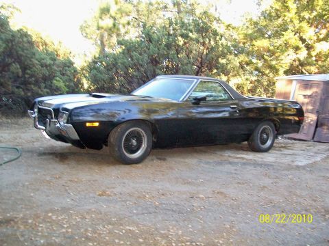 1972 Ford Ranchero - A black 1972 Ford Ranchero is parked outdoors with trees in the background. The vehicle has a hood scoop and aftermarket wheels.