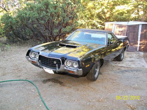1972 Ford Ranchero - Black 1972 Ford Ranchero with hood scoops sits on a dirt lot near a wooden shed.
