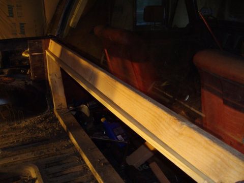 1978 Ford Bronco - The interior of a vehicle shows red seats and a blue bottle on the floor, with wooden framing visible.