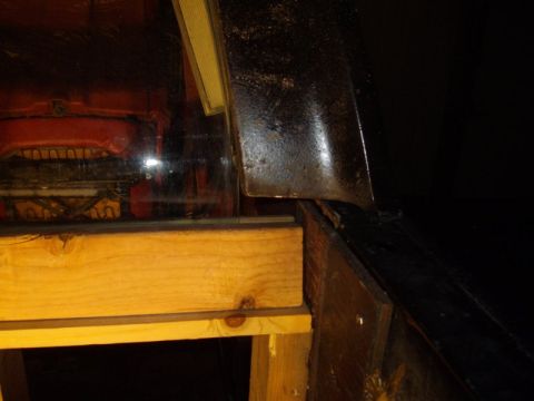 1978 Ford Bronco - Dark shop close-up of a piece of side glass resting on a wooden 2x4 stand next to a black-painted body panel, showing the gap between the g…