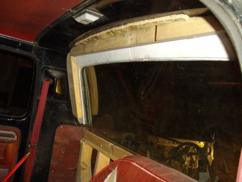 1978 Ford Bronco - Interior view of a truck cab looking rearward at a custom half-cab rear window installation, with a wood-framed opening built up from raw l…