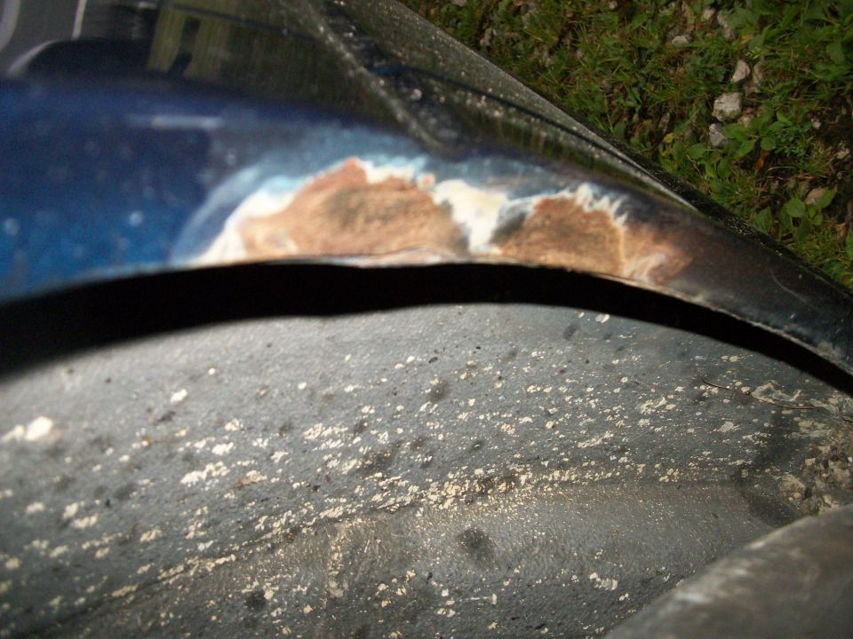 Rust and paint damage on blue car's fender edge near wheel arch