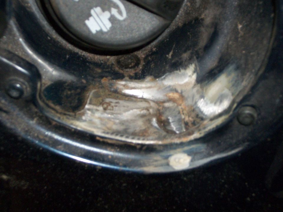 Fuel filler recess of a blue car with scraped paint, bare metal and rust around the gas cap