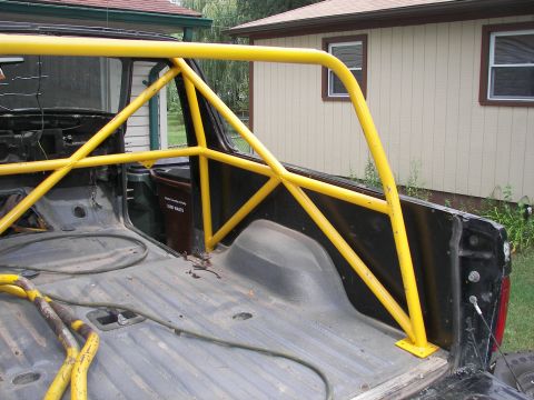 1988 Ford Bronco - The interior of a pickup truck bed shows a yellow roll cage and a trash can.