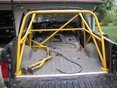 1988 Ford Bronco - Rear view of a black pickup truck with a yellow roll cage installed in the bed and a cracked windshield.