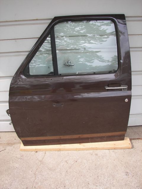 1988 Ford Bronco - A single brown vehicle door rests on wooden planks against a white wall.