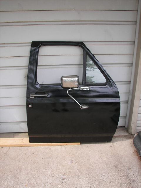 1988 Ford Bronco - A detached black truck door, likely for a Ford Bronco, is shown leaning against a wall.