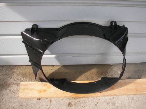 1988 Ford Bronco - Black plastic radiator fan shroud with mounting tabs, resting on wood planks against a corrugated wall.