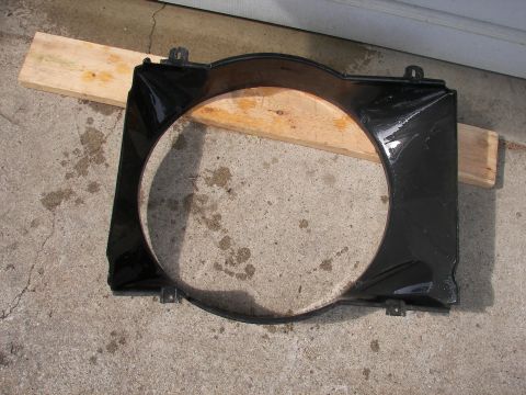 1988 Ford Bronco - A black radiator fan shroud is shown resting on a wooden plank over a concrete surface.