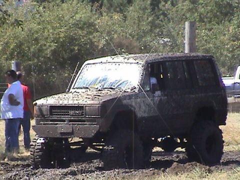 1994 Ford Explorer - This heavily mud-splattered Isuzu SUV navigates a rough terrain, likely during a mud drag event.