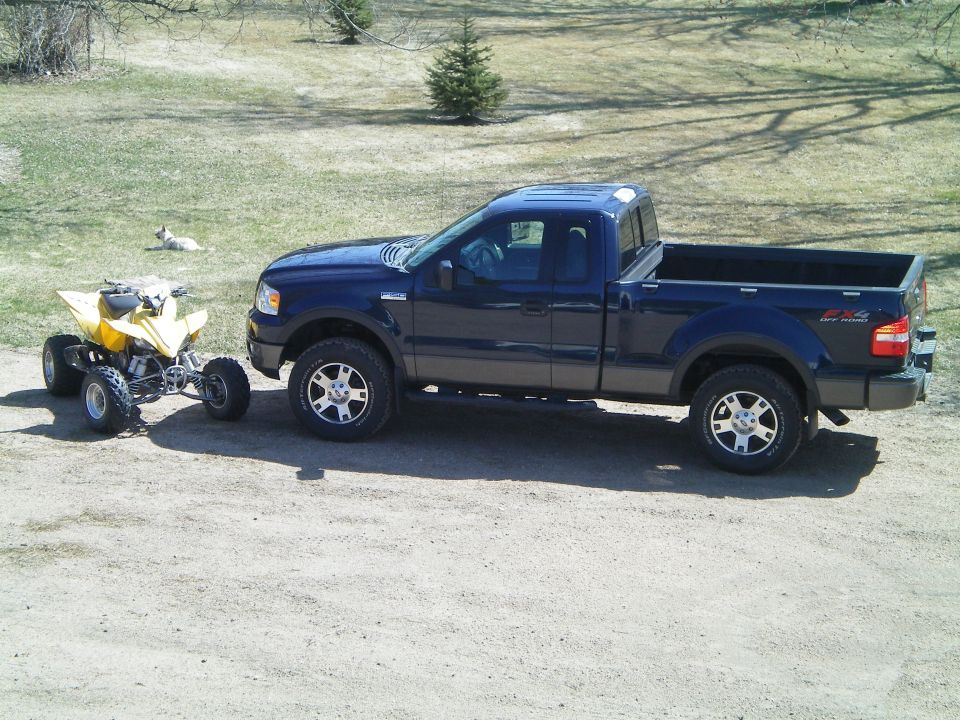 Side view of a dark blue 2005 Ford F-150 pickup truck towing a yellow ATV