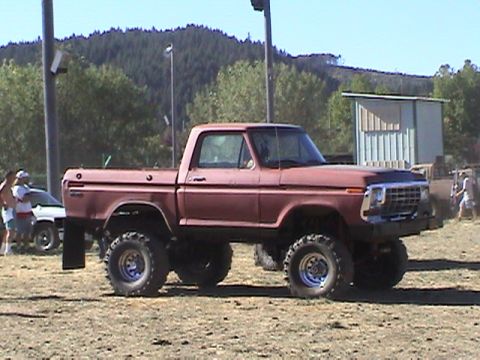 1994 Ford Explorer - A lifted pickup truck sits on a dirt lot under a clear sky, with trees and a building in the background.