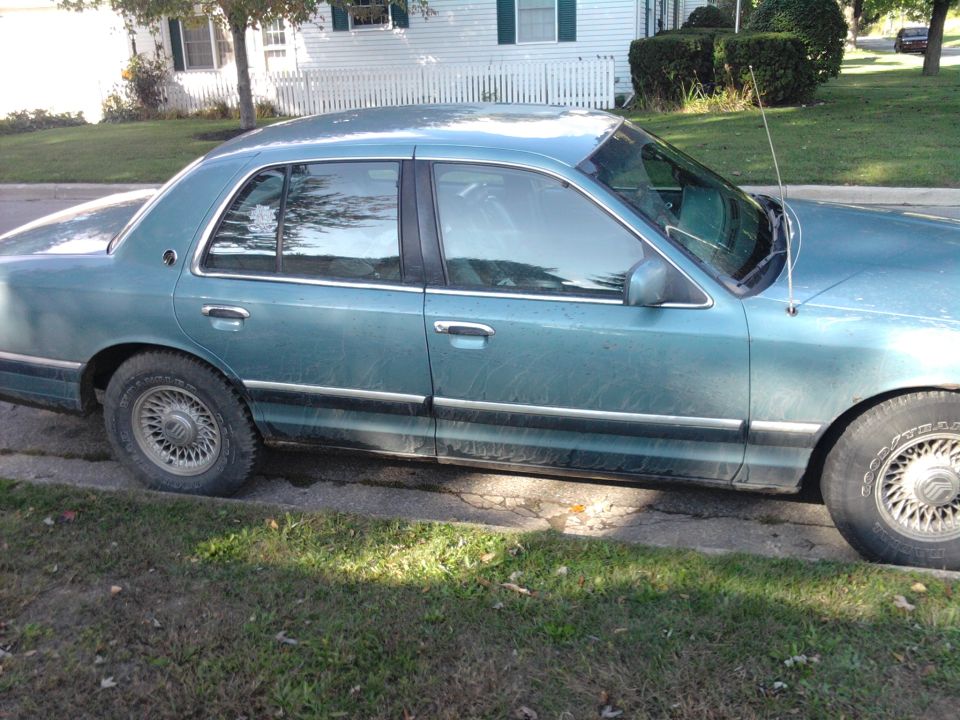 Side view of a teal sedan parked on a street. It has chrome trim and wire-style hubcaps