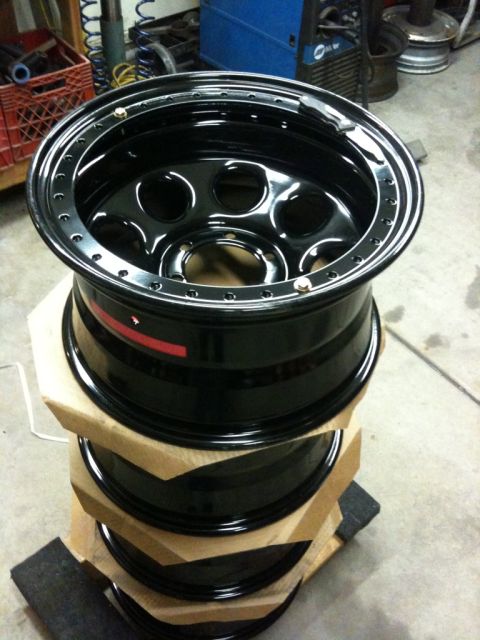 Suzuki Samurai - Four black rims are stacked on top of each other, with one rim showing a red stripe.
