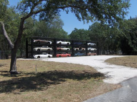 1979 Chevrolet Camaro - A collection of vehicles is stored on a multi-tiered rack under a tree.