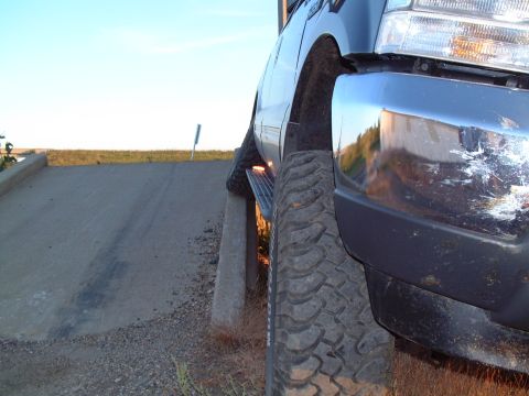 1986 Ford Bronco - A truck is parked on a concrete curb, showing its tire and scratched chrome bumper.