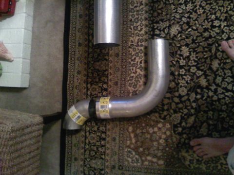 1990 Ford Bronco - Two sections of exhaust pipe are laid out on a patterned rug, with yellow labels visible on one piece.