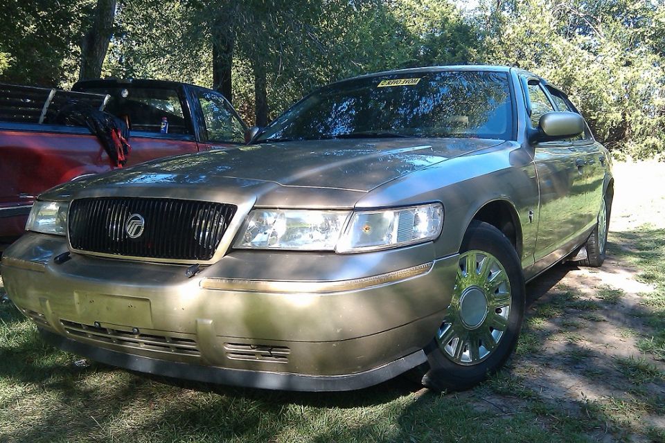 Gold Mercury Grand Marquis parked next to a red pickup truck, front 3/4 view