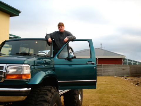 1996 Ford Bronco - A man leans on the open door of a green 1996 Ford Bronco, which features lifted suspension and large tires.