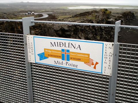 1996 Ford Bronco - Sign marks the Mid-Point between continents, with two cars on a road in the background.