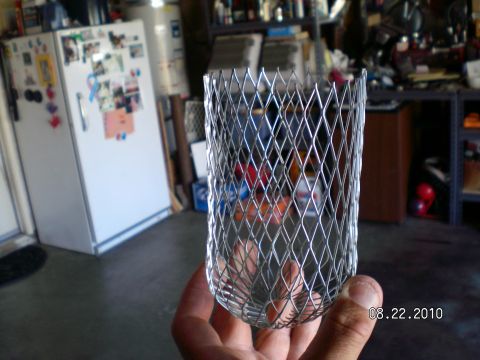 1996 Ford Bronco - A metal mesh part is held in a hand in front of a garage scene with a refrigerator.