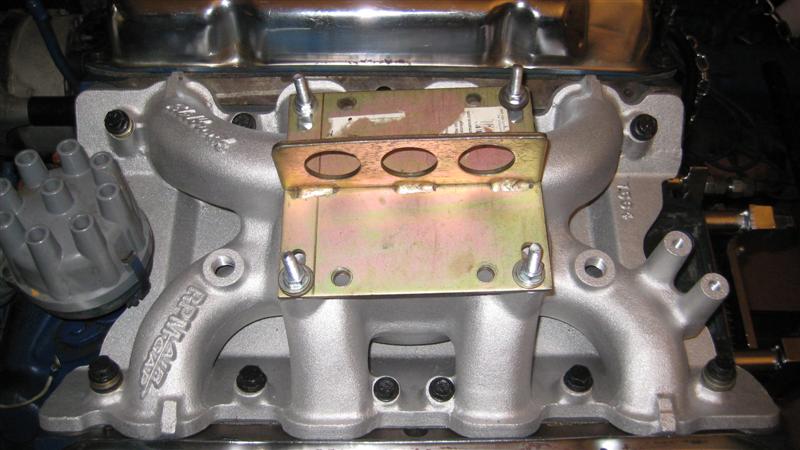 Silver aluminum intake manifold with a yellow metal bracket and three oval cutouts