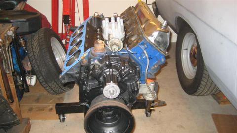 1968 Ford Ranchero - Engine assembly on a stand, partially obscured by a car's body and a spare tire.