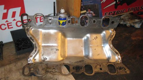 1968 Ford Ranchero - An engine intake manifold sits on a workbench, with a can of WD-40 and a box of bolts nearby.