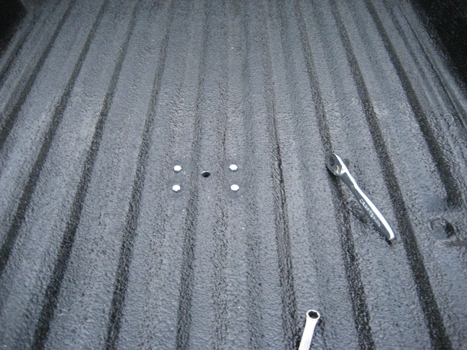 Truck bed liner with four mounting holes and two wrenches. SUPERMOTORS.NET logo visible