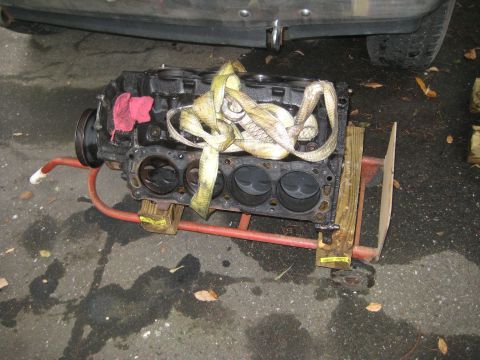 1988 Ford Bronco - Engine block on a dolly, ready for transport or repair, with a portion of a vehicle overhead.