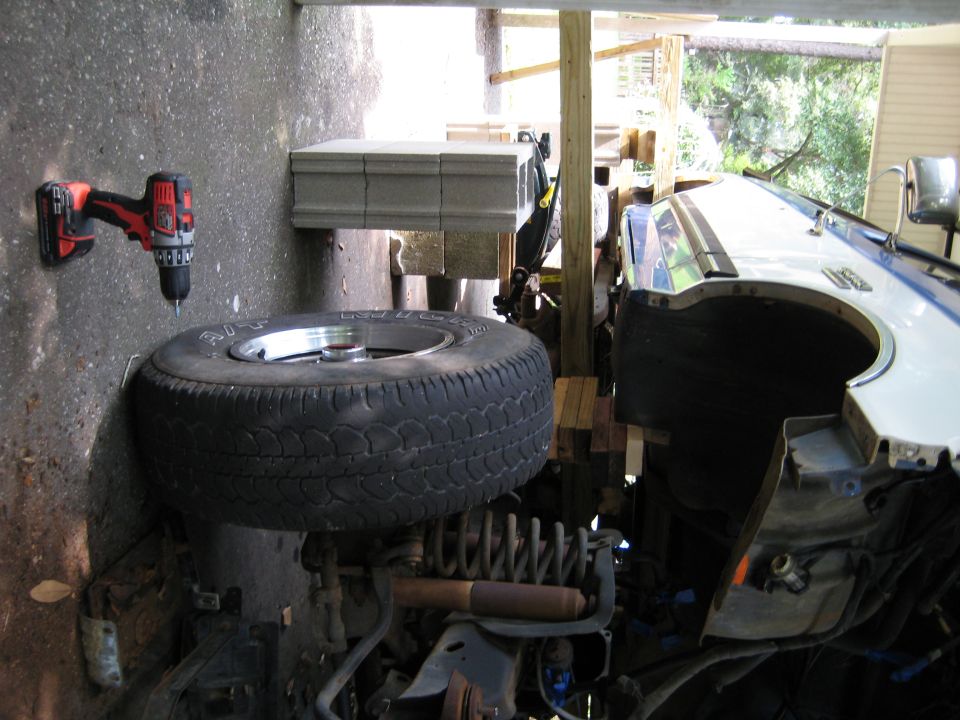 Drill on wall next to spare tire and vehicle suspension parts