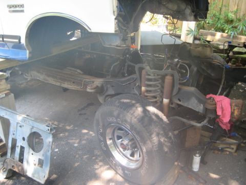 1988 Ford Bronco - The chassis of a 1988 Ford Bronco is shown from the side, with its front wheel and suspension exposed during a rebuild.
