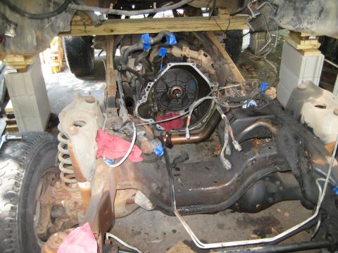 1988 Ford Bronco - The engine and transmission area of a vehicle are visible, with the transmission removed and the chassis supported by blocks for repair.