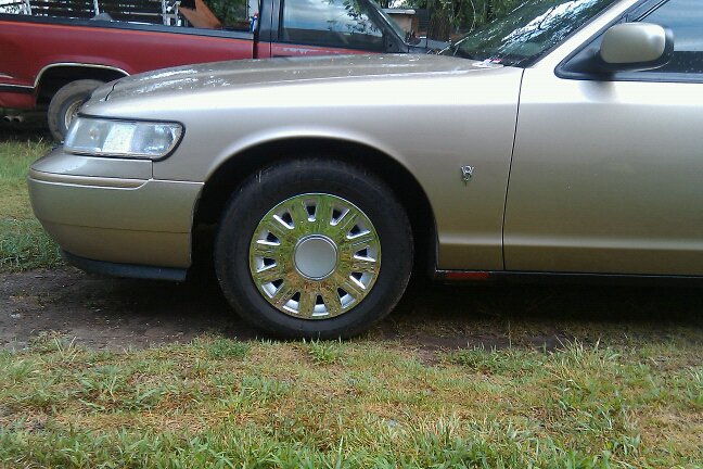 Front quarter of gold sedan, parked next to red pickup truck. Shows wheel and headlight