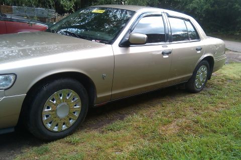 2000 Mercury Grand Marquis - A gold 2000 Mercury Grand Marquis is parked on a grassy area next to another vehicle.