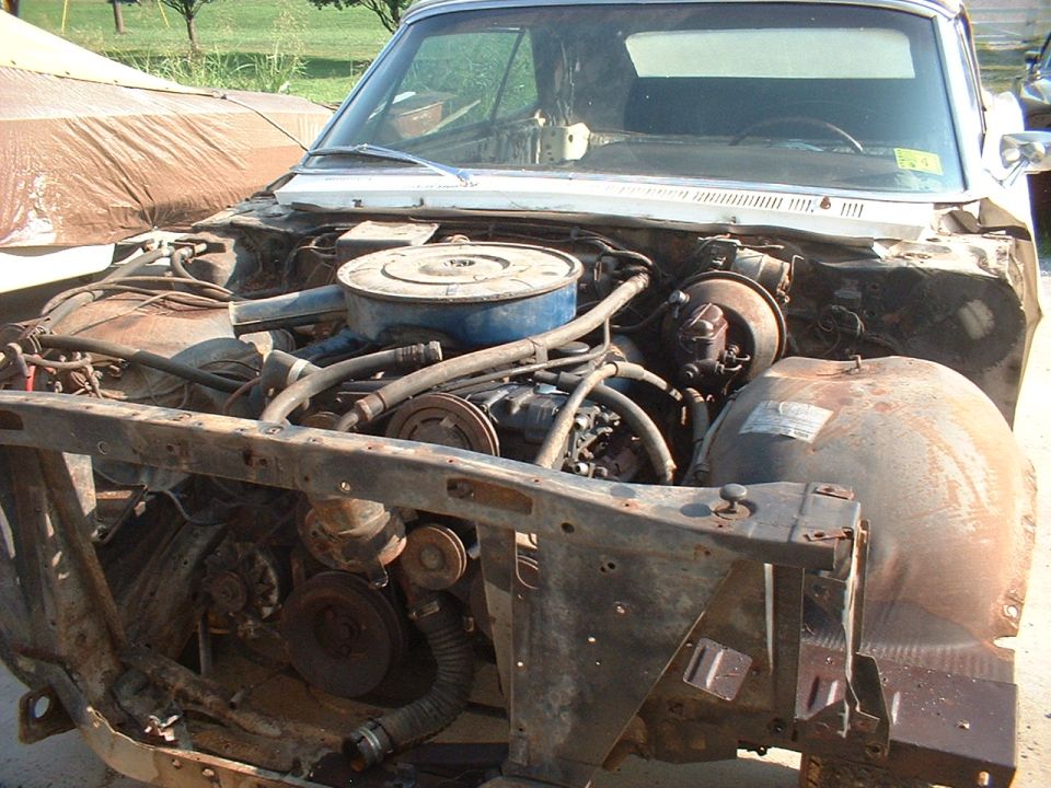 Classic car with front sheet metal removed, exposing a V8 engine with blue air cleaner during restoration