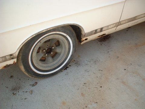 1967 Ford Galaxie - The rear wheel and lower body panel of a white vehicle show significant rust and wear.