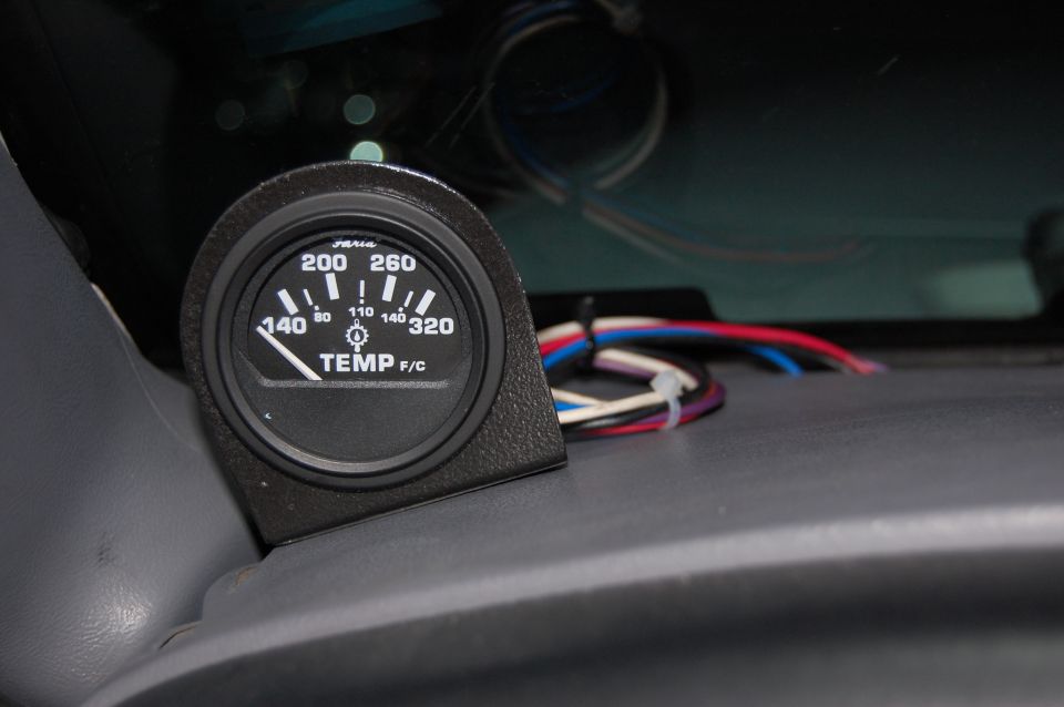 Aftermarket temperature gauge with wiring harness, mounted on a dashboard