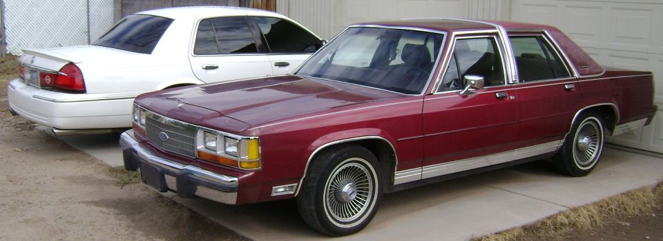 Burgundy full-size Ford four-door sedan, 3/4 front view, wire wheel covers and whitewall tires