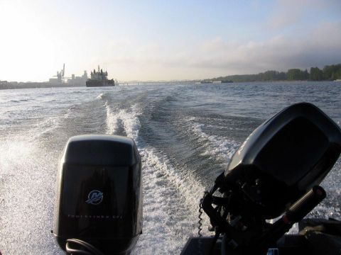 1996 Ford Bronco - View from a boat moving through the water, showing two outboard motors and a distant barge.