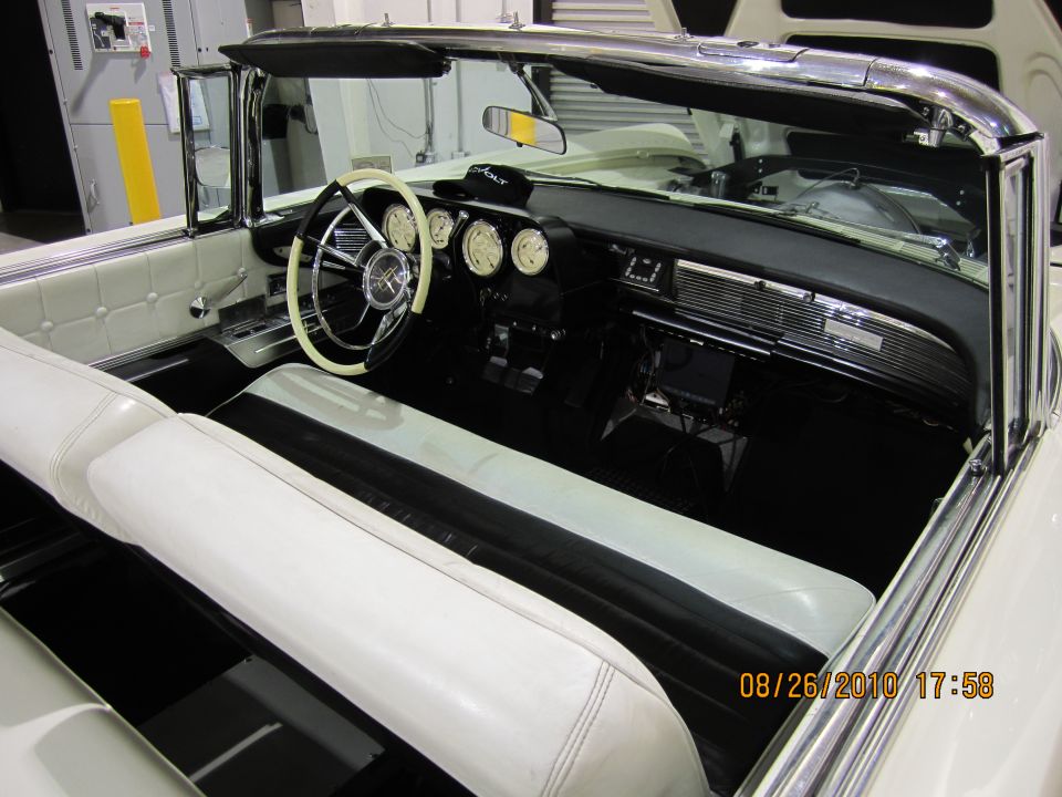 Interior view of a classic convertible with white and black seats, a two-tone steering wheel, and multiple gauges