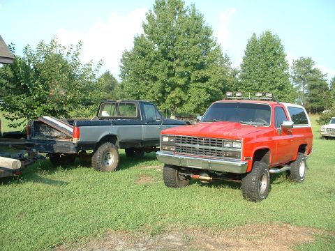 1994 GMC Suburban - Two trucks are parked on a grassy lawn with trees in the background.
