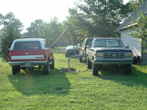 1994 GMC Suburban - Two lifted trucks and a red and white SUV are parked on a grassy lawn in front of a building.
