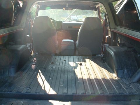 1994 GMC Suburban - The interior of a red SUV shows two rows of seats and a cargo area with a ribbed floor, illuminated by sunlight.