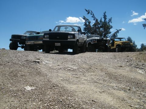 1982 Ford Bronco - Several off-road vehicles are parked on a dirt hill under a blue sky. The lead vehicle is a white Ford truck.