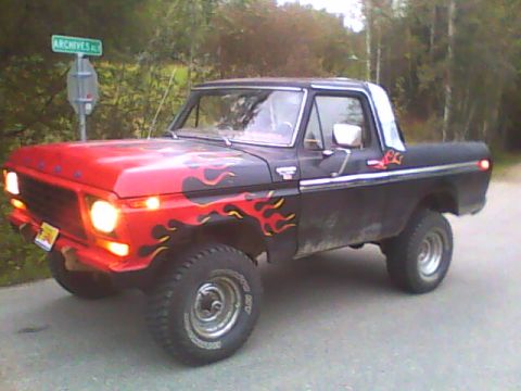 1978 Ford Bronco - Three-quarter front view of a black and red half-cab Ford Bronco with orange and yellow flame graphics across the hood and body sides, head…