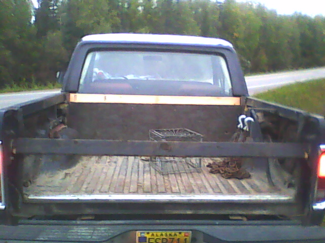 Rear of a dark Ford Bronco half-cab with wood bed and Alaska plate JSP711