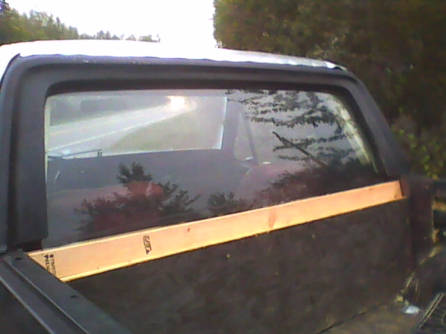 Black Bronco half cab rear window with wood board along lower glass edge, parked outdoors.