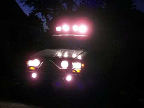 1988 Ford Bronco - An SUV is illuminated by numerous bright auxiliary lights mounted on its roof and front bumper.