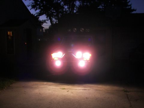 1988 Ford Bronco - Vehicle with bright headlights illuminated at night in a driveway.